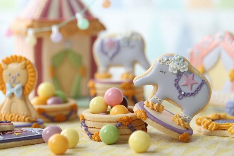 Сладости в пастельных тонах лежат на столе — отдельно или в небольших чашах для печенья — рядом с глазированным печеньем в форме животных.