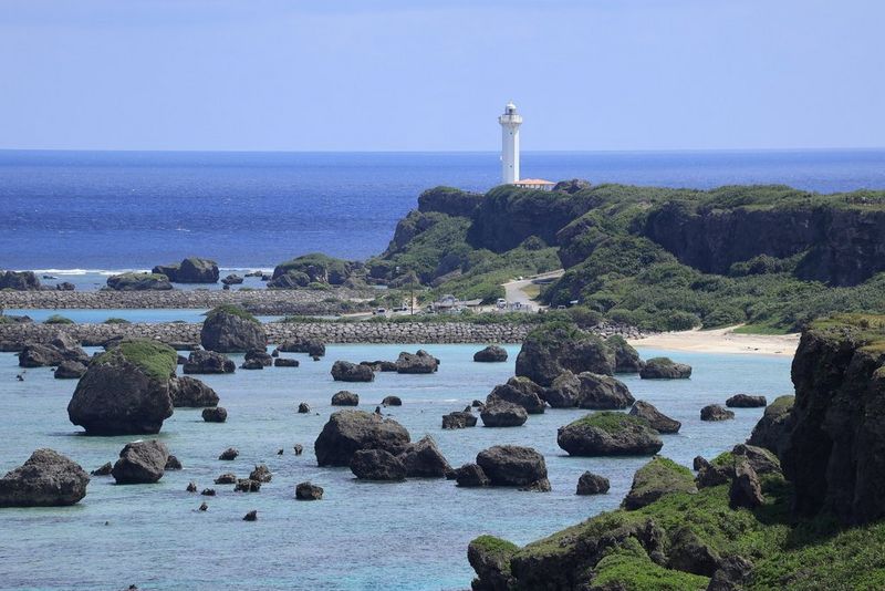 Vista mucho más cercana del faro al final del promontorio, con una costa rocosa y grandes rocas en el agua debajo de él. Se ha fotografiado con un teleobjetivo Canon RF-S 55–210mm F5–7.1 IS STM a una longitud focal de 210 mm.