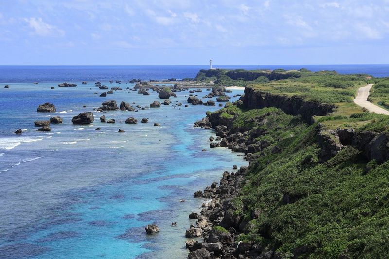 Vista de una lengua rocosa cubierta de hierba que se adentra en el mar, con un faro al final en la distancia. Se ha fotografiado con un teleobjetivo Canon RF-S 55–210mm F5–7.1 IS STM a una longitud focal de 55 mm.