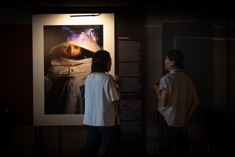 В приглушенном свете выставочного зала на ЭКСПО 2025 в Осаке две женщины рассматривают напечатанный портрет артиста в сценическом костюме.