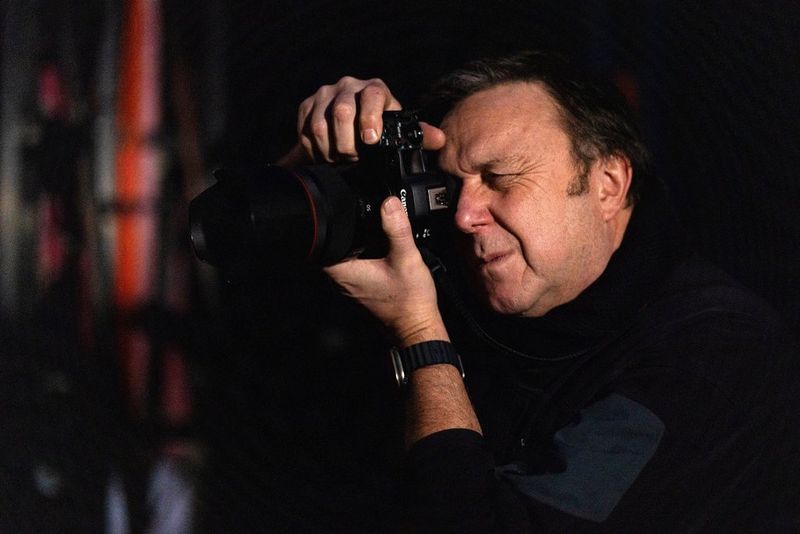 Клайв Бут подносит камеру Canon EOS R5 Mark II к лицу, готовясь с делать снимок.