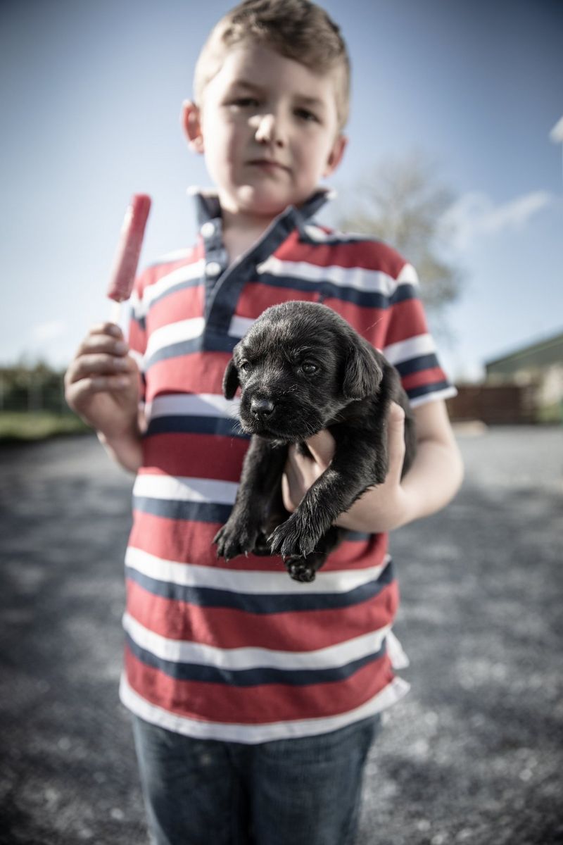 Young Robbie Brown holding a black Labrador puppy at his family home on Islay captured by Clive Booth on the Canon EOS 5DS R.