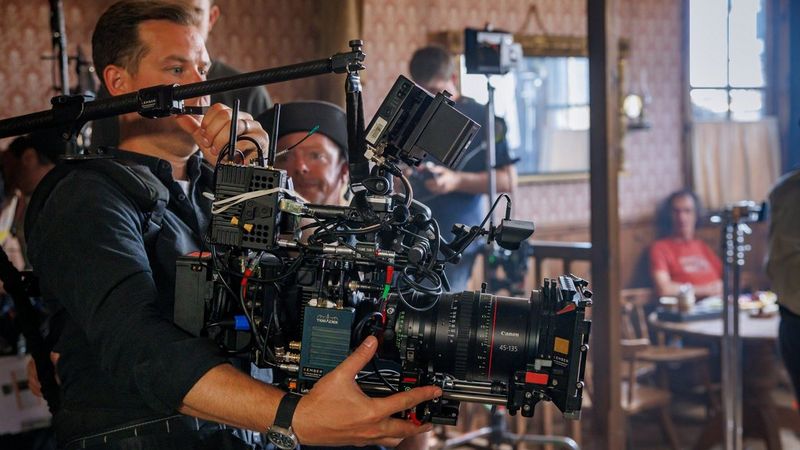 A man adjusts a large camera rig on the set of an old-fashioned Western bar.