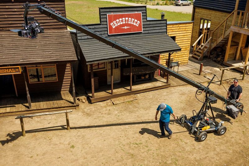 An overhead shot of a man pulling a tall camera rig down the street of a Western town set.