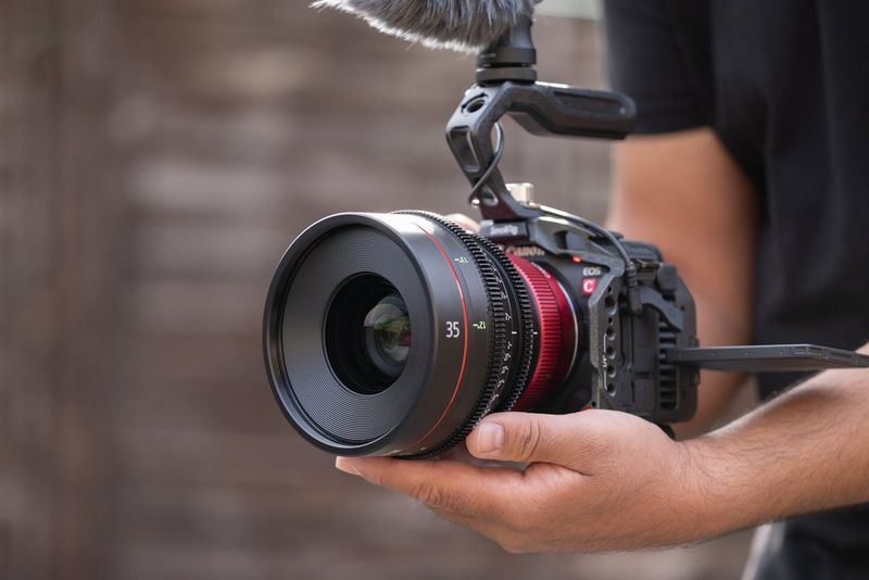A pair of hands holds a Canon EOS R5 C with a CN-R Prime lens attached to it. 