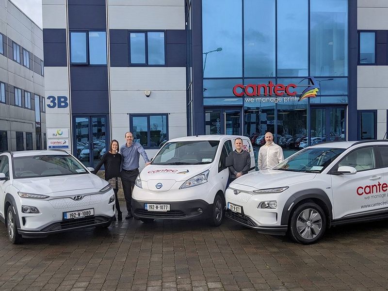 Two white electric cars and an electric van, with three men and a woman standing with them. Behind them are the offices of Cantec Ireland.