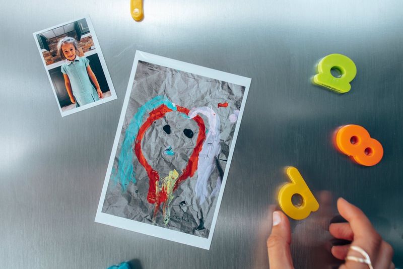 Распечатка рисунка в формате фотокарточки, выполненная на магнитной бумаге, прикреплена на холодильник. Вокруг нее прикреплены магнитные цифры и буквы.