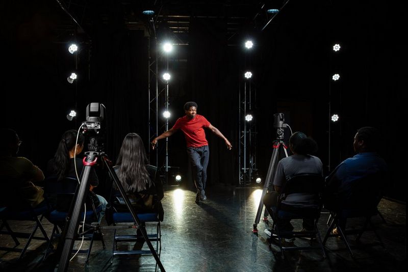 Two Canon PTZ cameras mounted on tripods directed at a person in red shirt. A few people in chairs watch the person perform.  