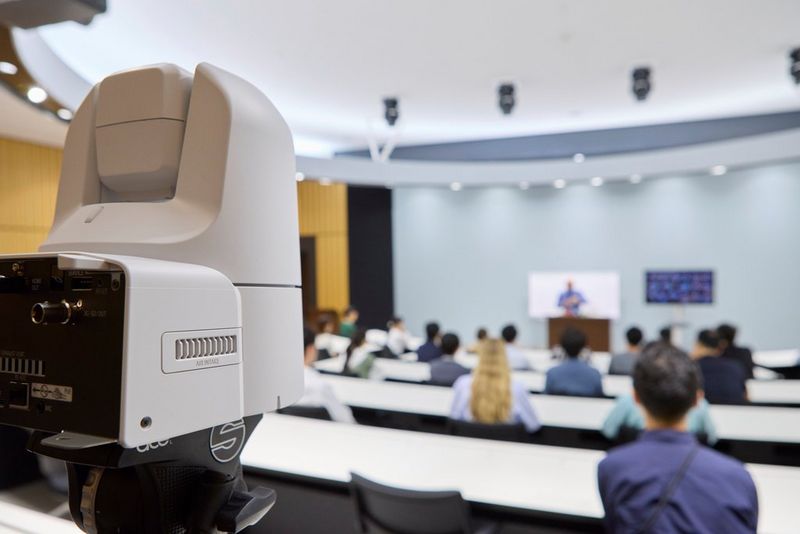 A Canon CR-N350 PTZ camera points towards the speaker at the front of a lecture hall.