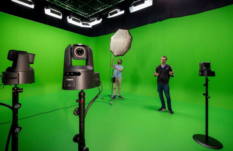 A green screen studio equipped with multiple Canon robotic cameras and professional lighting, with two people preparing for a video production.