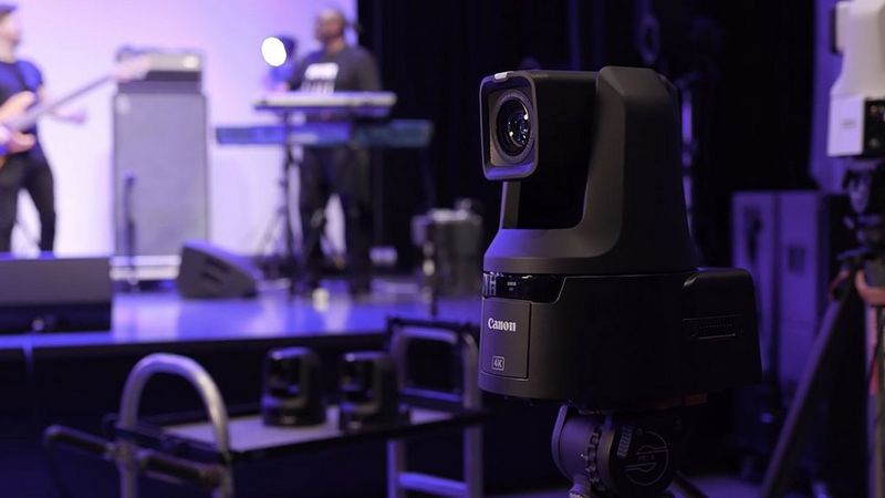 Une caméra Canon CR-N500 baignée dans une lumière violette. En arrière-plan, on aperçoit un groupe de musiciens sur scène.
