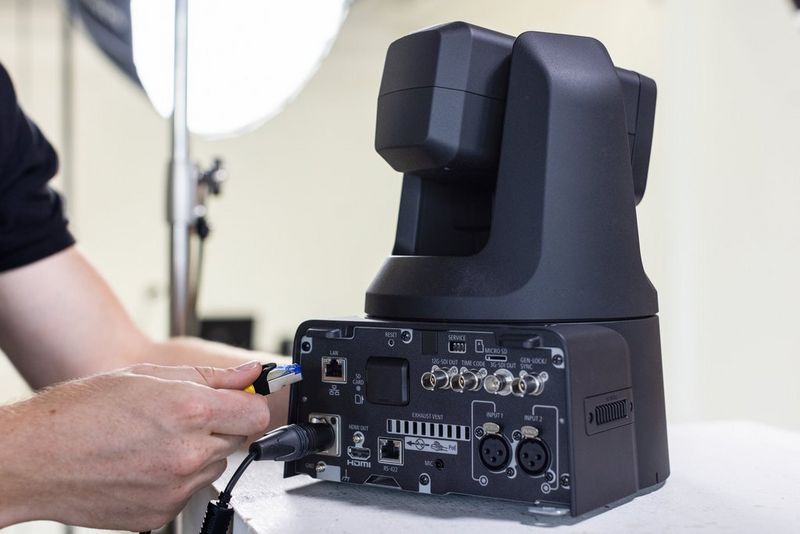 A hand plugs in a cable into the LAN port of a Canon CR-N700 PTZ camera. 