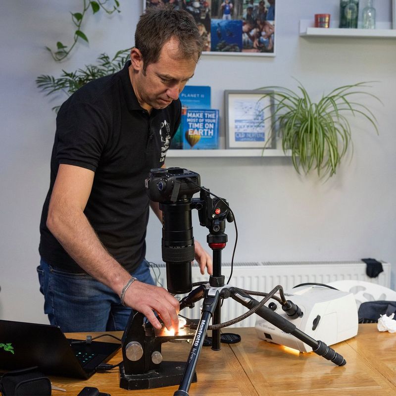 Dr Jamie Craggs at his wooden kitchen table, observing samples on a slide using a specially adapted Canon camera.