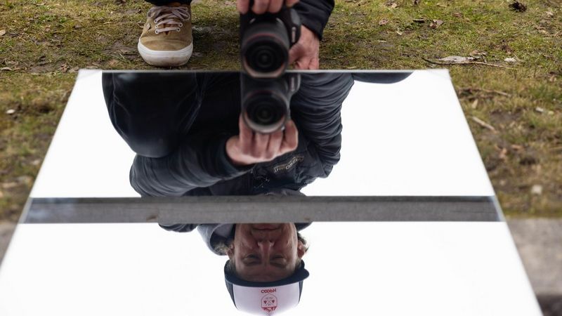 Action photographer Lorenz Holder holding his Canon EOS R5 Mark II close the surface of a mirror placed on the ground, preparing to take an action photograph of a trick reflected in the mirror.