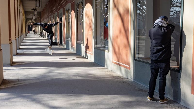 Action photographer Lorenz Holder stands against a mirrored wall with the shadows of the arches of a colonnade stretching into the distance, photographing the reflection of a skateboarder in action.
