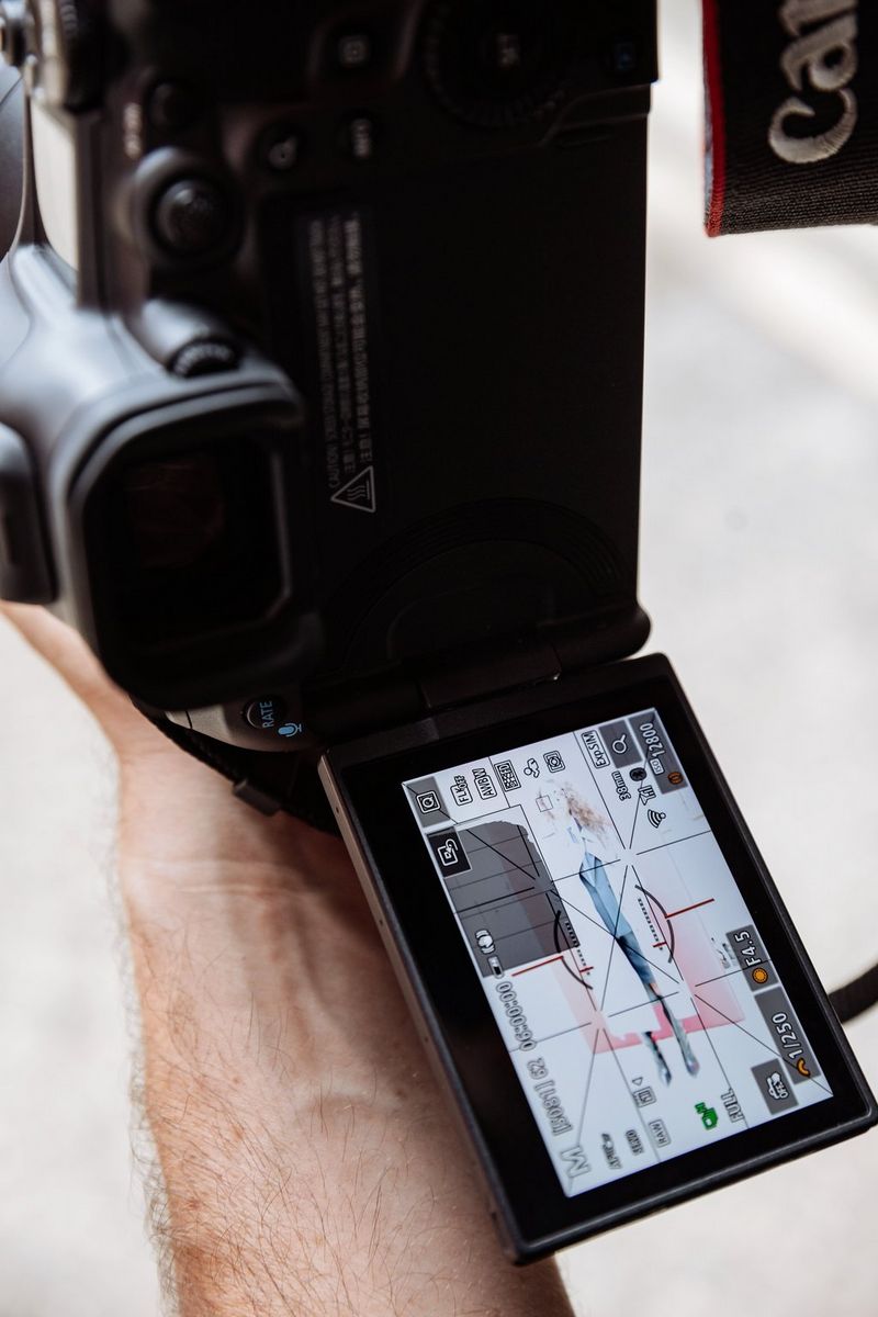 The vari-angle screen of a Canon EOS R5 Mark II showing a full-length portrait of a model in a light-coloured overcoat with a wide range of image information displayed over it.