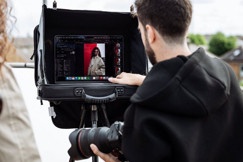 Portrait photographer Samuel Sarfati checks a photo in Capture One on the screen of a laptop on a stand on an urban rooftop, holding a Canon camera in one hand. 