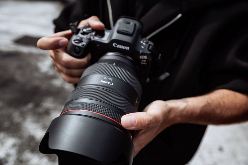 Portrait photographer Samuel Sarfati adjusts the control ring on a Canon RF 28-70mm F2L USM lens attached to a Canon EOS R5 Mark II held in his other hand.