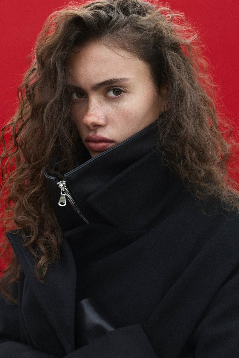 Portrait photo taken by Samuel Sarfati on a Canon EOS R5 Mark II showing a model in a dark coat against a red background, with her features well-exposed and detail in the dark coat also clear.