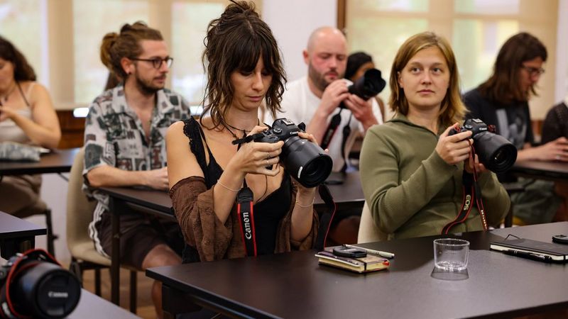 Students sat at a row of desks with Canon EOS R System camera and note books at the Canon Student Development Programme.