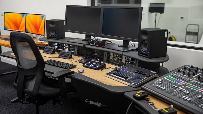 An office table and chair. On the table are several screens, speakers and control panels for editing and managing a studio.