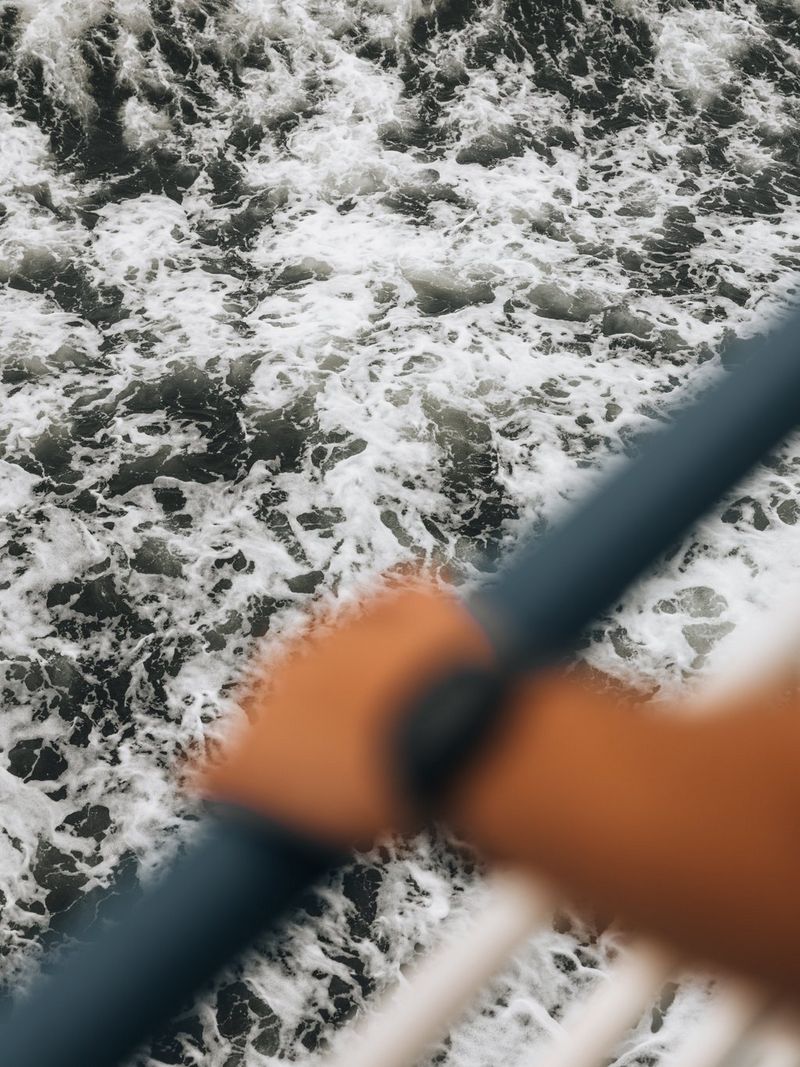 A person's out-of-focus arm holding the railings of a boat, ocean waves captured sharply in the background. Travel photo taken by Cuno de Bruin on a Canon EOS R5 Mark II.