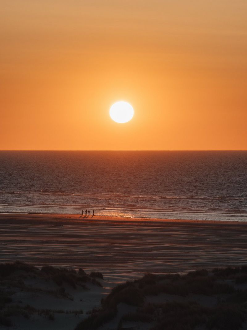 The sun going down over the sea near the island of Terschelling, with people bathed in the orange glow on the shoreline. Travel photo taken by Cuno de Bruin on a Canon EOS R5 Mark II.