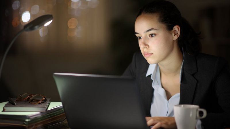 Woman in business wear working on a laptop late at night.