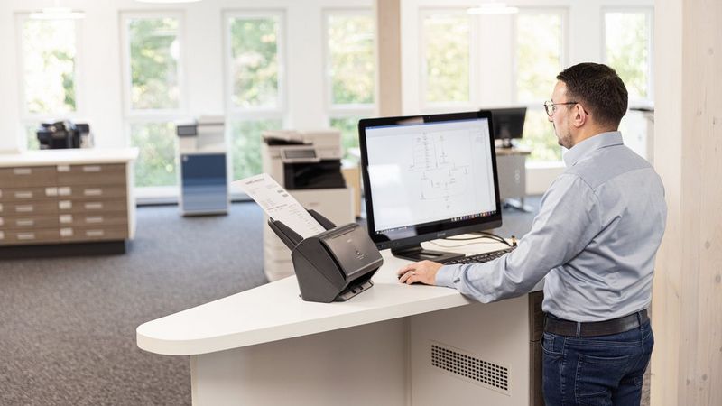 Man in front of desk with laptop and document scanner