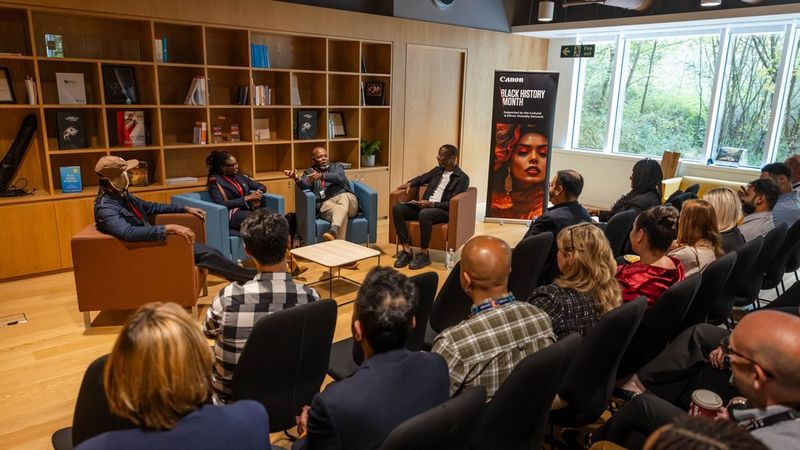 A panel discussion taking place in Canon’s library for Black History Month. The audience, with back to camera, sit and listen to four speakers.