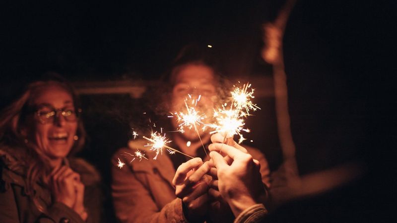 A blurry photo of two people, with a third out of shot, holding sparklers