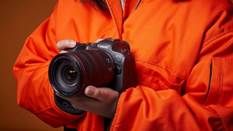 Fotograf in einer leuchtend orangefarbenen Jacke mit einer spiegellosen Canon EOS R6 Kamera mit einem Canon Objektiv.