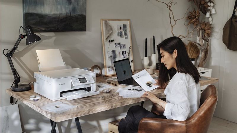 Ein PIXMA Drucker an einem Arbeitsplatz zu Hause; eine Person verwendet einen Laptop, um Dokumente auszudrucken.