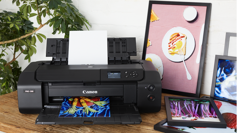Drucker der PIXMA PRO Serie auf einem Schreibtisch mit farbenfrohen Fotodrucken.