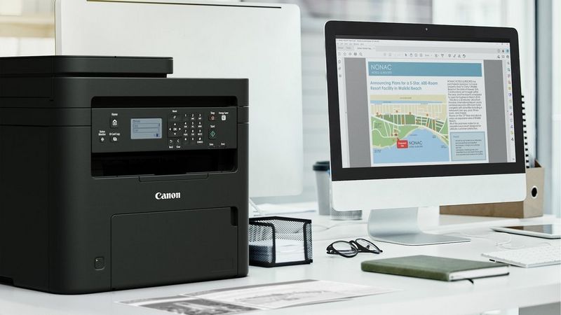 Canon i-SENSYS MF272dw Drucker auf einem Schreibtisch neben einem Computer im Homeoffice.