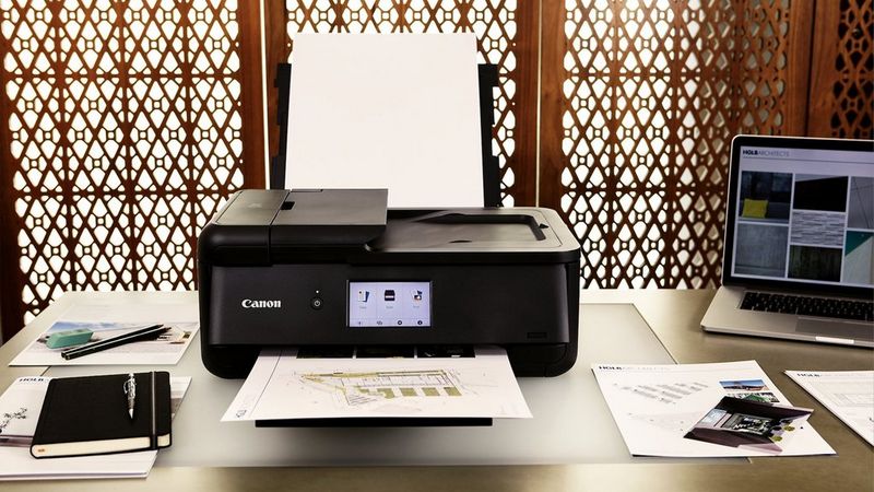 Canon PIXMA TS9550a Drucker auf einem Schreibtisch beim Drucken eines Dokuments neben Laptop und Briefpapier