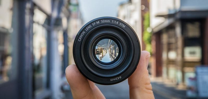 Eine Person, die ein Canon EF-M 32mm f/1.4 STM Objektiv hält, während sie auf einer Straße steht.