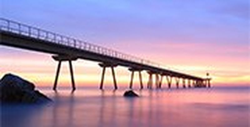 A long jetty, viewed from water level at dusk, stretches into the sea.