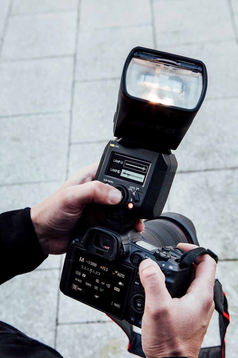 Mano di un fotografo mentre regola le impostazioni sulla parte posteriore di Canon Speedlite EL-1 collegato a una fotocamera EOS R5 che tiene nell'altra mano.