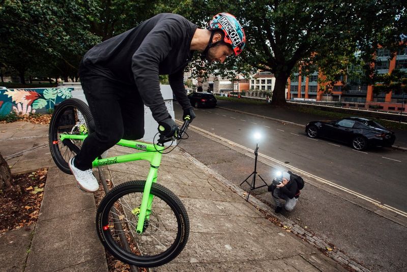 Een stuntrijder op een felgroene fiets balanceert op zijn voorwiel en wordt gefotografeerd met twee Canon Speedlite EL-1-flitsers.
