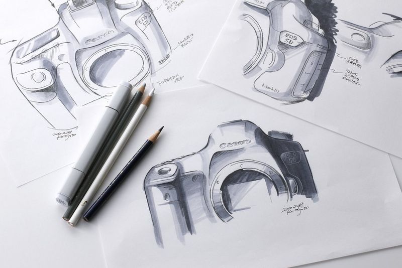 Potloden en een pen liggen op een vel met schetsen van ontwerpconcepten van Canon EOS 5D camera's.