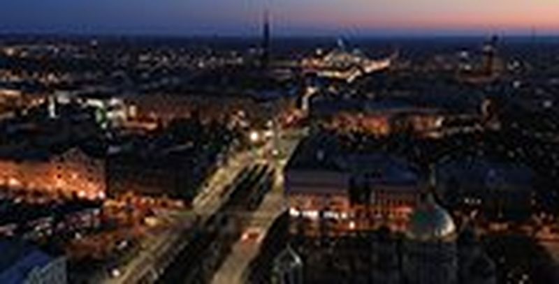 An aerial view of a city at night, many buildings illuminated below a dark blue sky streaked with pink.