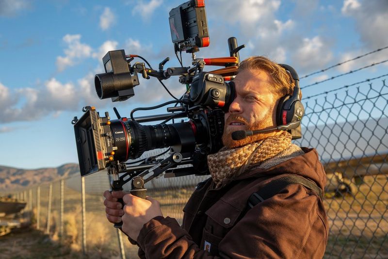 Un homme portant un casque et des vêtements chauds filme en extérieur, une Canon EOS C300 Mark III à l'épaule.