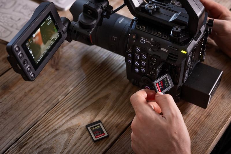A user's hands change a memory card in a Canon EOS C400 pro video camera on a wooden desktop.
