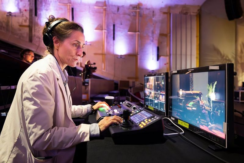 Sarah Thomas Moffat zit aan een control desk in een auditorium en bedient een Canon RC-IP1000-controller en kijkt naar een monitor voor haar.