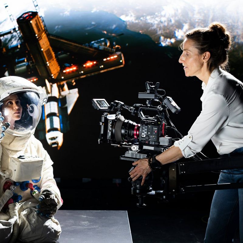 Cinematographer Sarah Thomas Moffat holds the Canon EOS C400 to film a woman in a space suit, with a satellite in the background