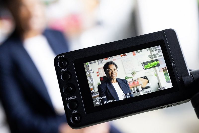 Lo schermo LCD di una videocamera Canon EOS C400 mostra le impostazioni in uso, incluso il profilo Canon Log 3, durante la ripresa di un'intervista, con il soggetto visibile sul display.