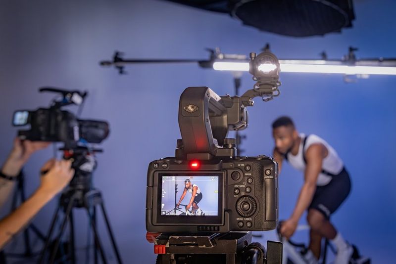 A man on a bicycle in a studio, with several Canon cameras filming him.