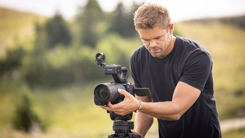 A user watches the camera's vari-angle screen as he adjusts the lens attached to a Canon EOS C50 camera on a tripod.