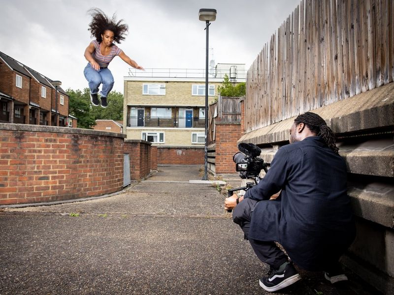 Een cinematograaf hurkt tegen een muur en gebruikt een Canon EOS C70 op een gimbal om een skateboarder te filmen, vastgelegd terwijl die een stunt in de lucht uitvoert.